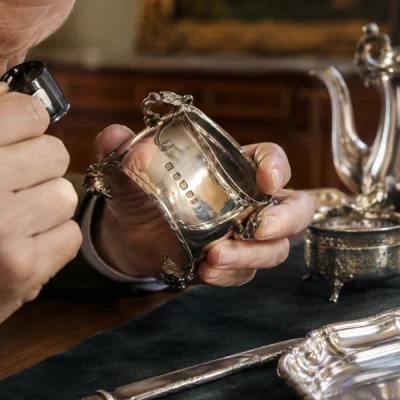 Expert examinant à la loupe les poinçons d'une pièce d'argenterie ancienne avant estimation